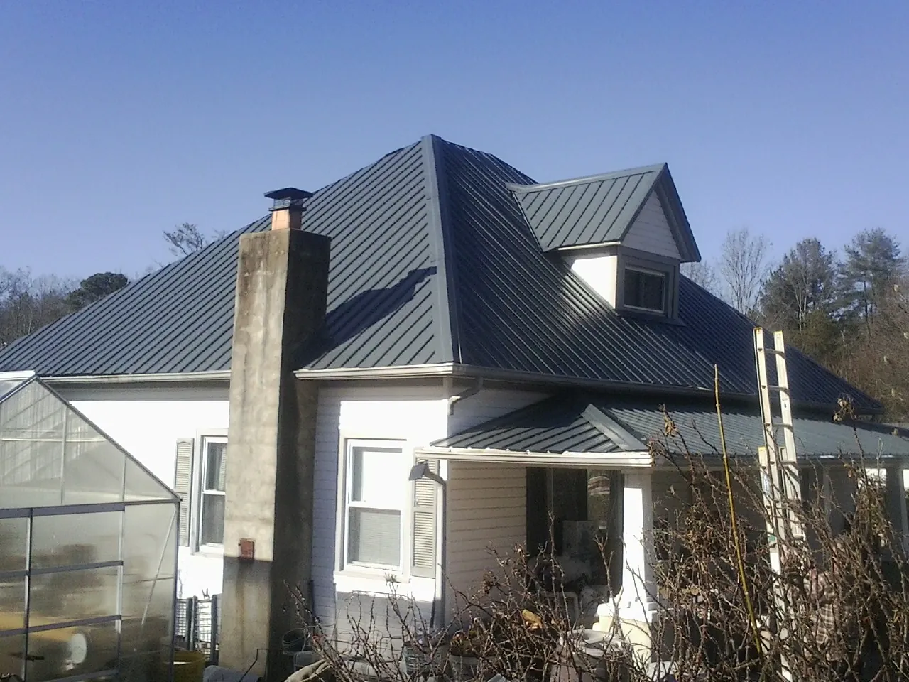 Dark blue standing seam metal roof on a white farmhouse with dormer — Slate & Tile Roof Repair by Roofing Brothers in Perkinston