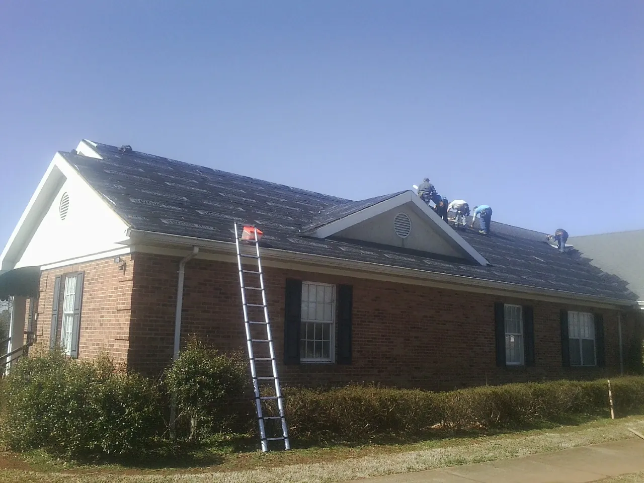 Crew tearing shingles off a brick ranch roof with a ladder set — Metal Roof Repair work by our crew in Perkinston