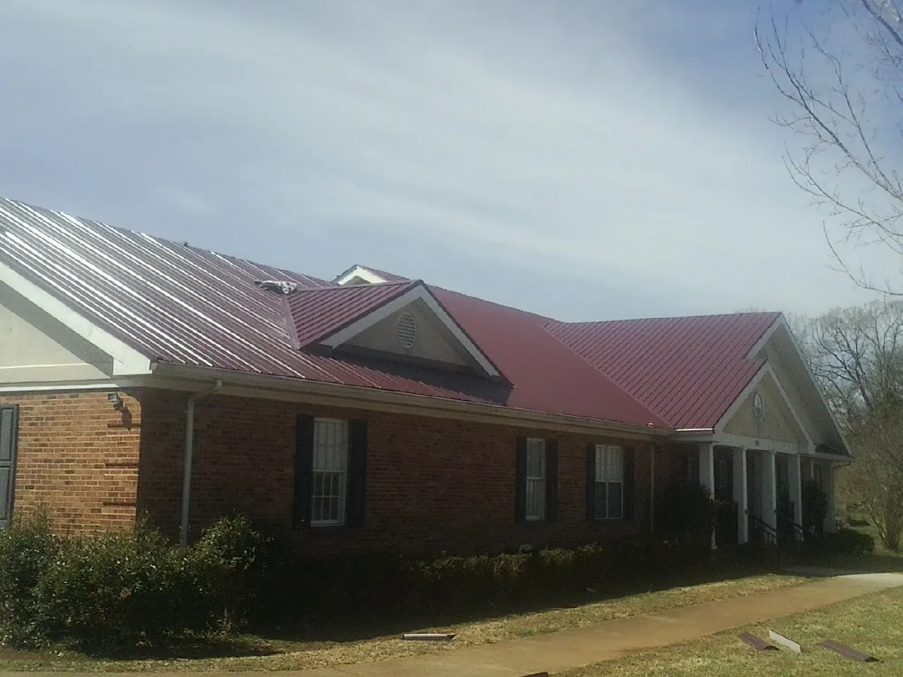 Red metal roof with gabled entries on a long brick building, from a Hail Damage Roof Repair job in Perkinston