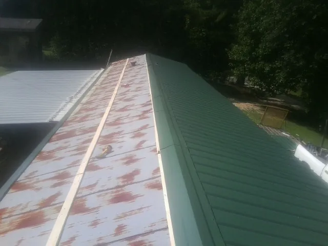 Old rusted panels beside newly installed green metal roofing — Wind Damage Roof Repair by Roofing Brothers in Perkinston