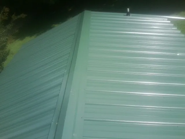 New green metal panels meeting at the ridge of a roof — Flat Roof Repair work by our crew in Perkinston