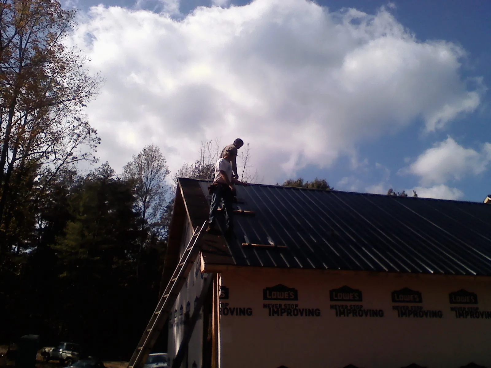 Roofer fastening dark metal panels high against a cloudy sky, from a Roof Inspection job in Perkinston