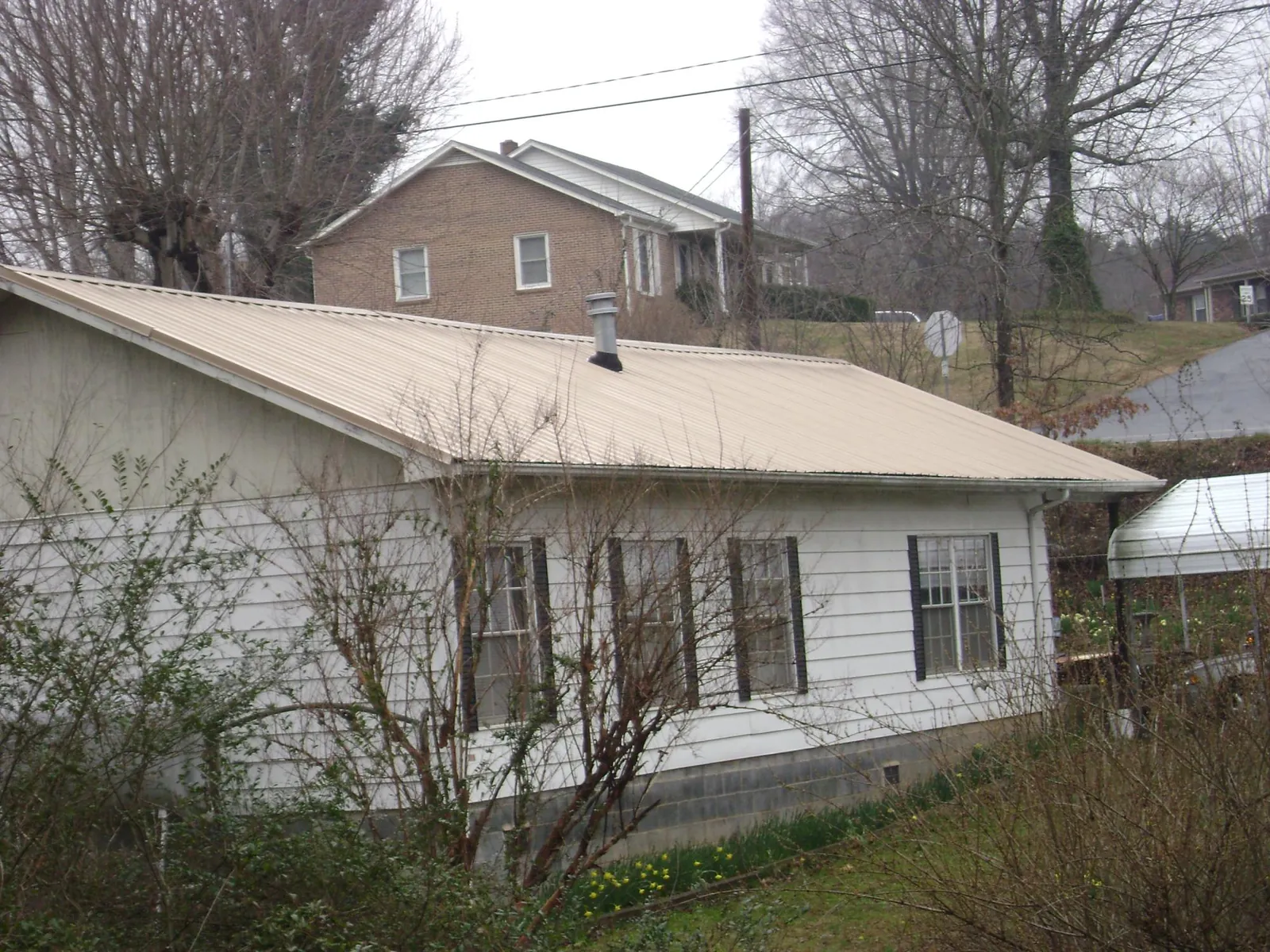 Tan metal roof on a white sided house set into a hillside — Commercial Roofing by Roofing Brothers in Perkinston
