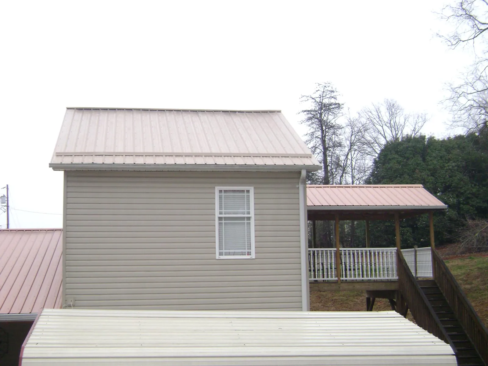 Tan metal roofs on a two story addition and attached porch, from a Roof Replacement job in Perkinston